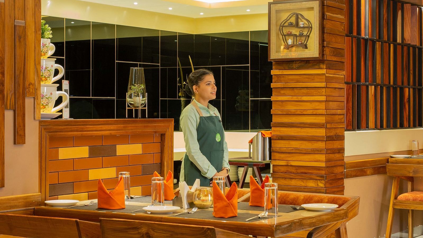 Interiors of Honeycomb Restaurant at Coral Reef Hotel & Spa in Port Blair featuring an attendant awaiting near the dining setting and warm lighting