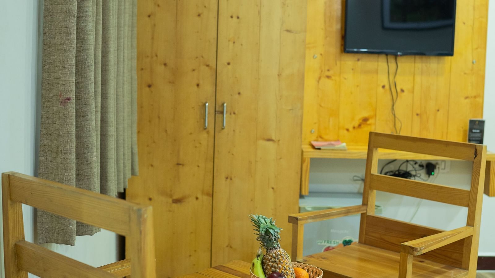 A small dining space with wooden chairs, wardrobe, and T.V., in a guest room at Daksh Resort & Amusement Park.