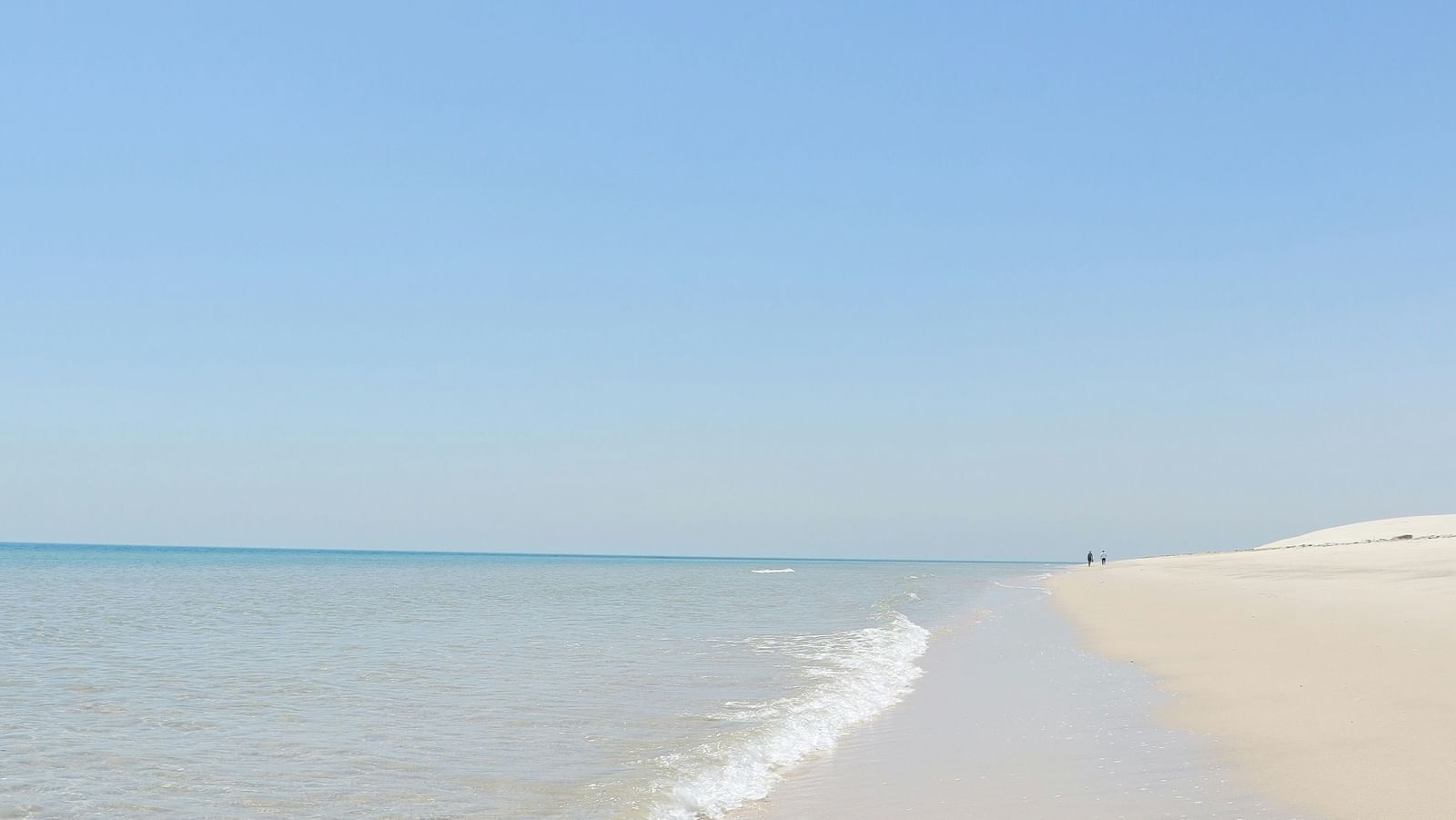  A calm, clear blue sky over a tranquil sandy beach with gentle waves lapping the shore.