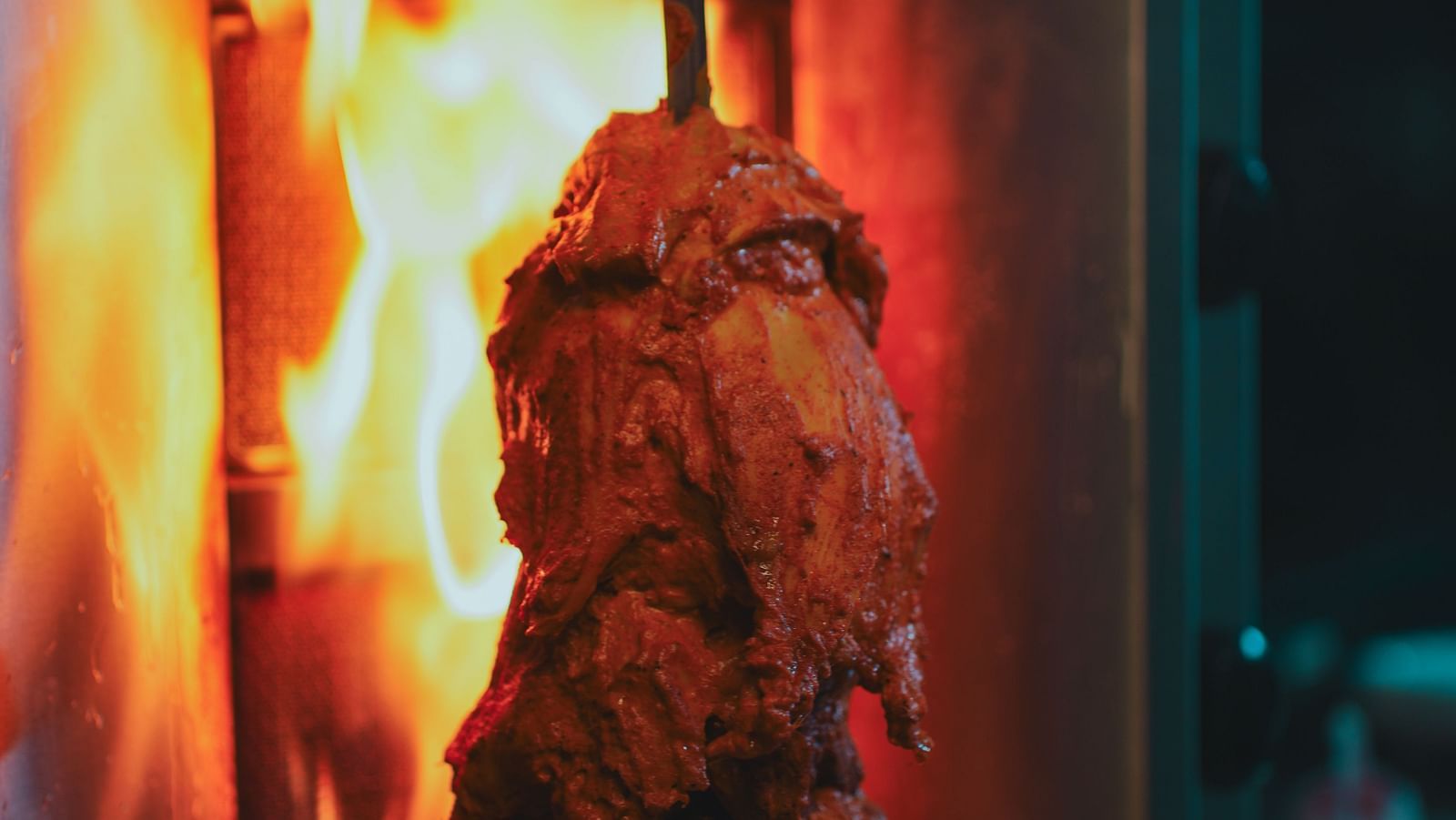 Shawarma meat roasting on a vertical spit over an open flame at D Café in Dip Holidays, showcasing the authentic and fiery cooking process.