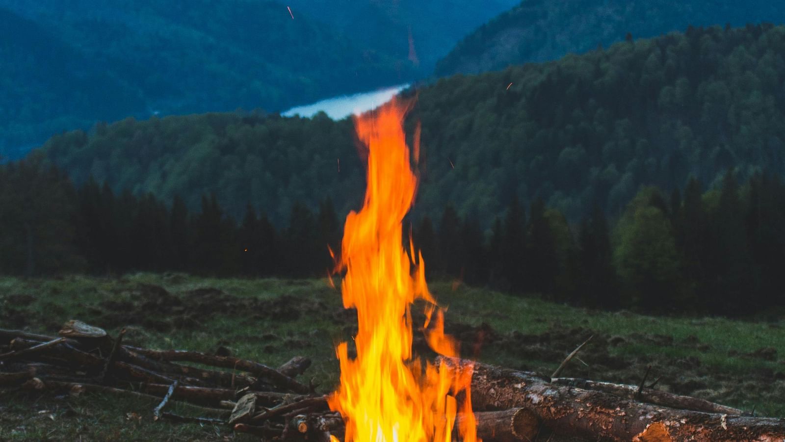A campfire burns brightly in a mountain landscape at dusk.