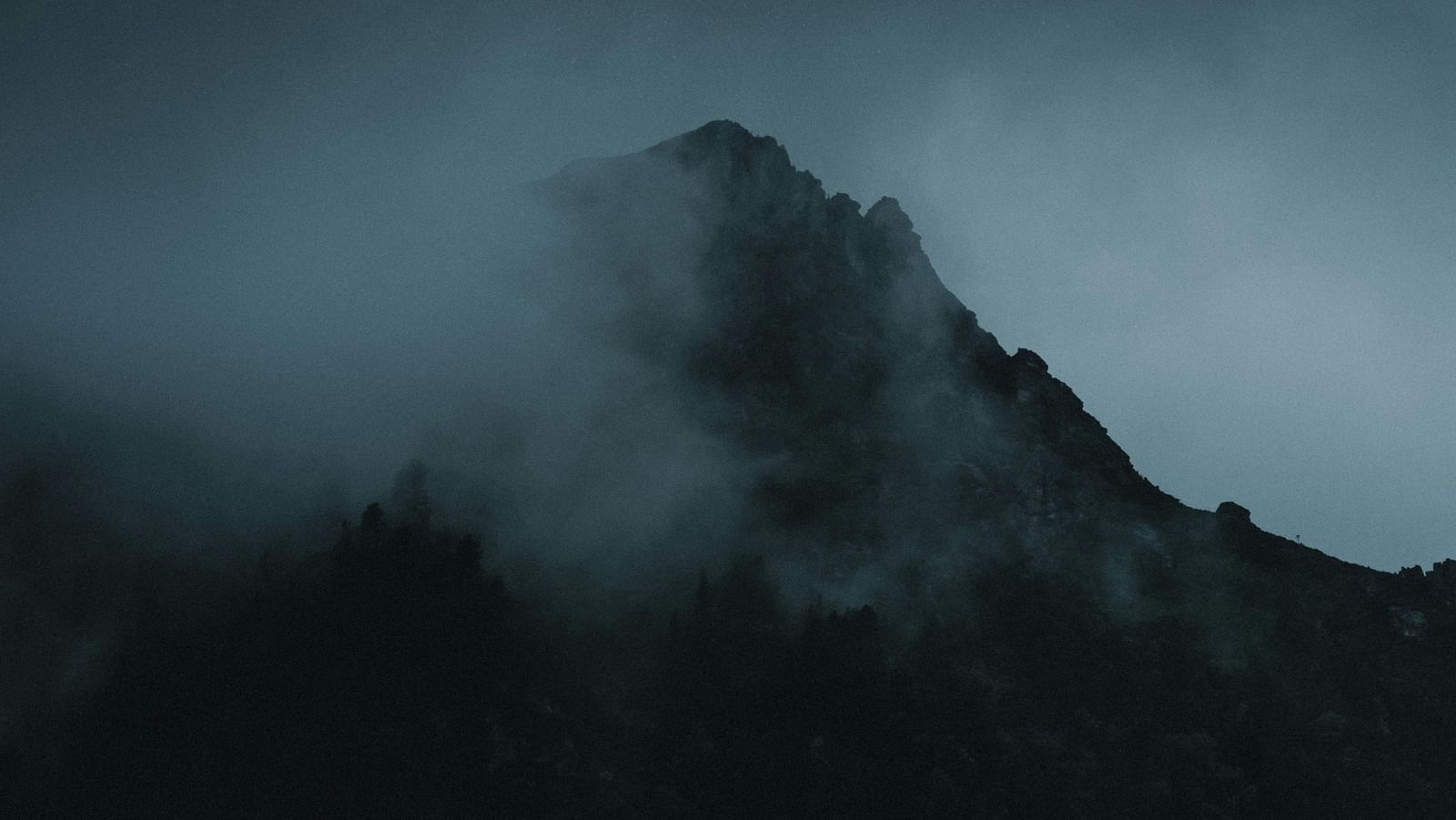 Misty mountain peak shrouded in clouds with a mysterious and moody atmosphere.