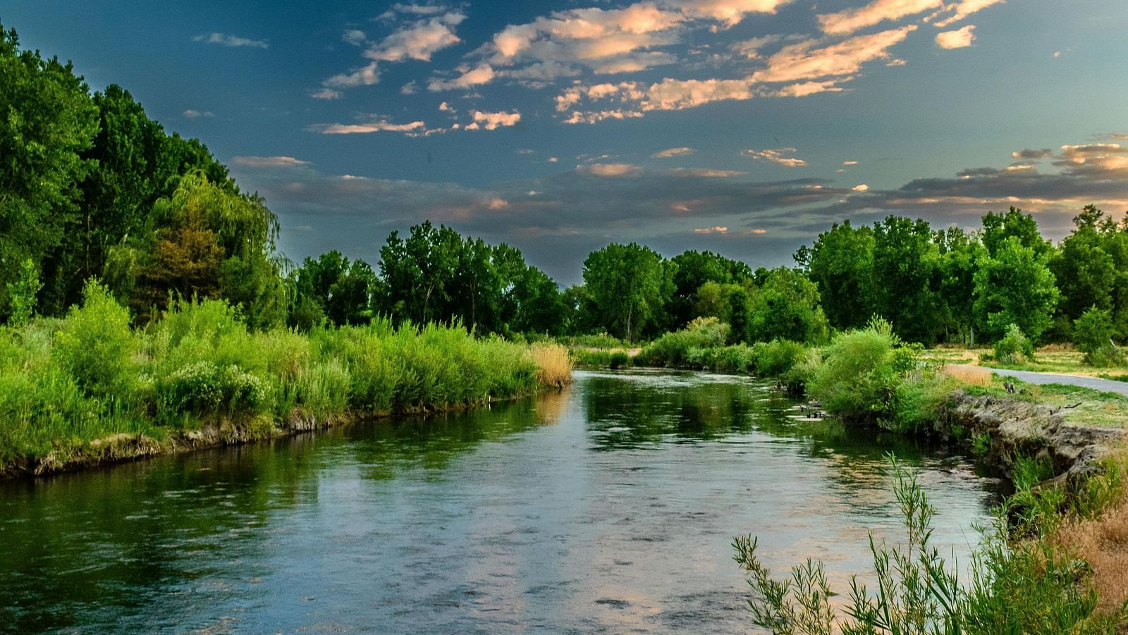 Serene river flowing through a verdant landscape under a colourful sunset sky.