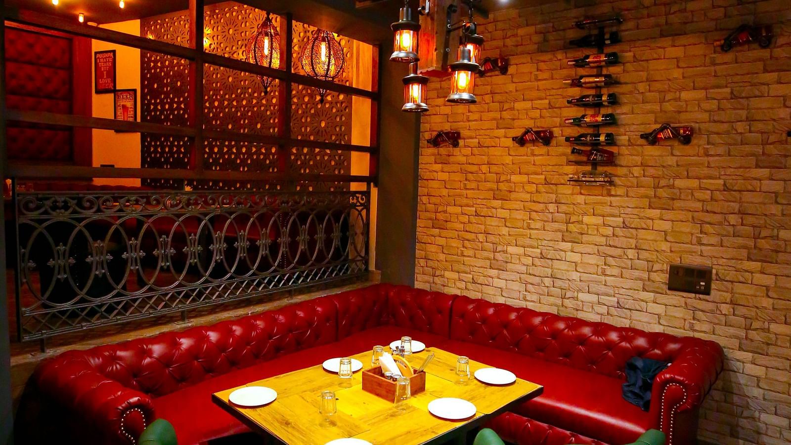 An intimate booth seating area with a plush red sofa and vintage-style lanterns in a restaurant setting - Hotel Moti Palace