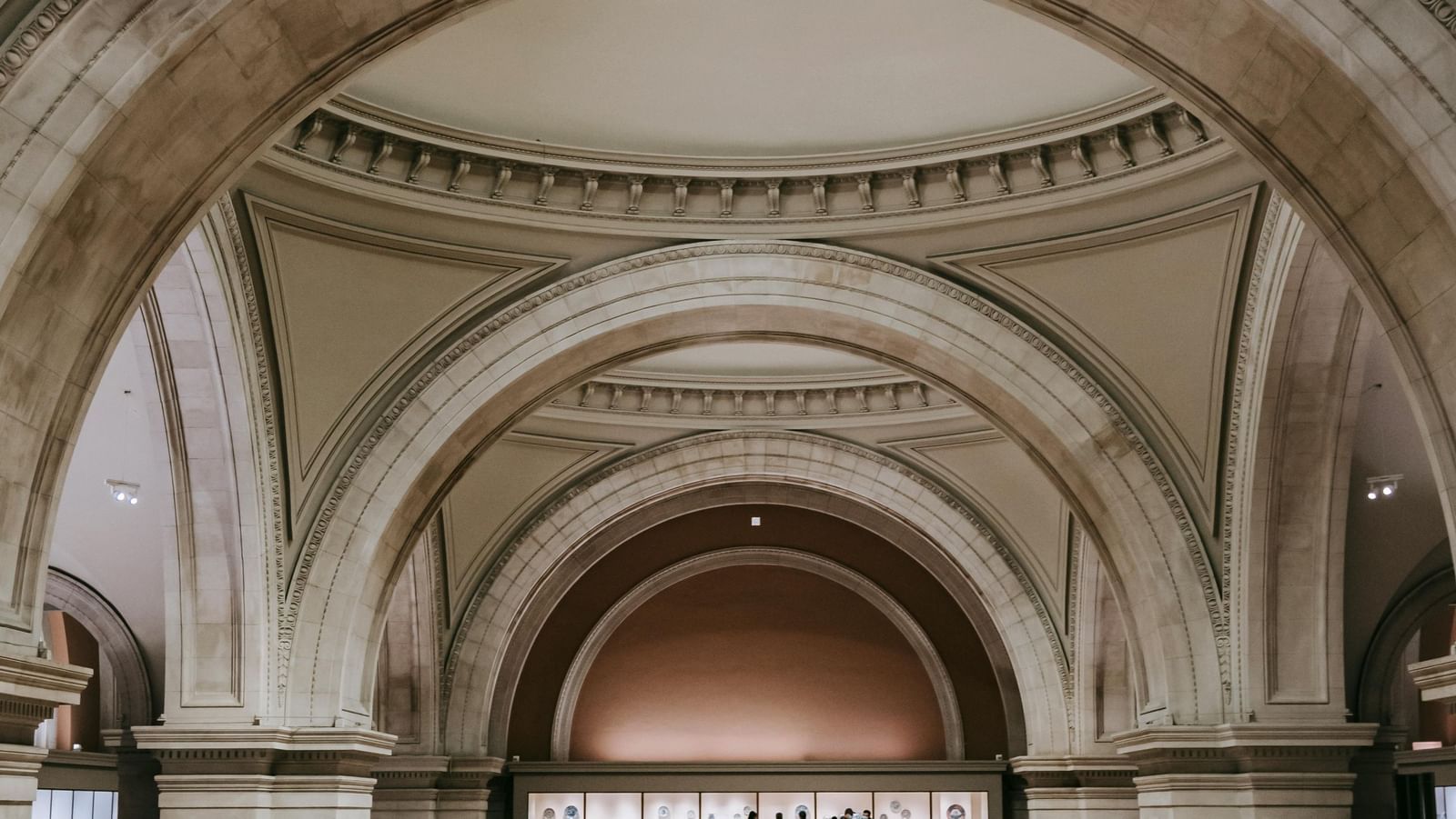 An elegant museum hall with high vaulted arches, marble details, and a wide walkway filled with visitors exploring the grand interior.