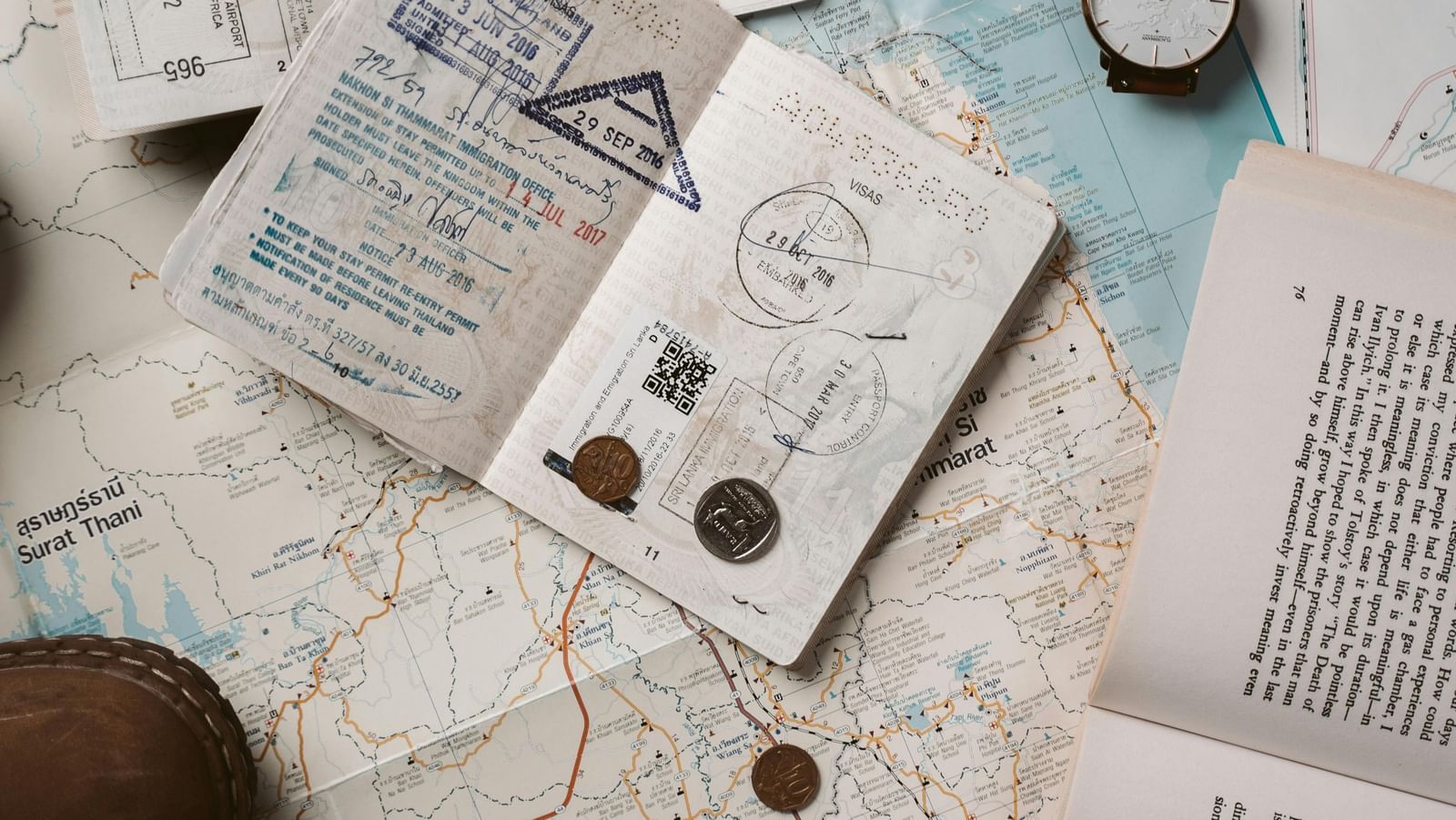 Travel documents, maps, coins, and headphones spread out on a surface, showing detailed preparation for a journey.