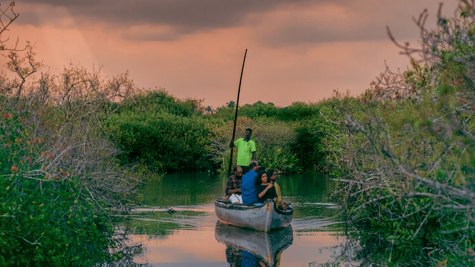 a family sitting on a boat with a boatsman rowing the boat on a river and different hues in the sky after the sunset