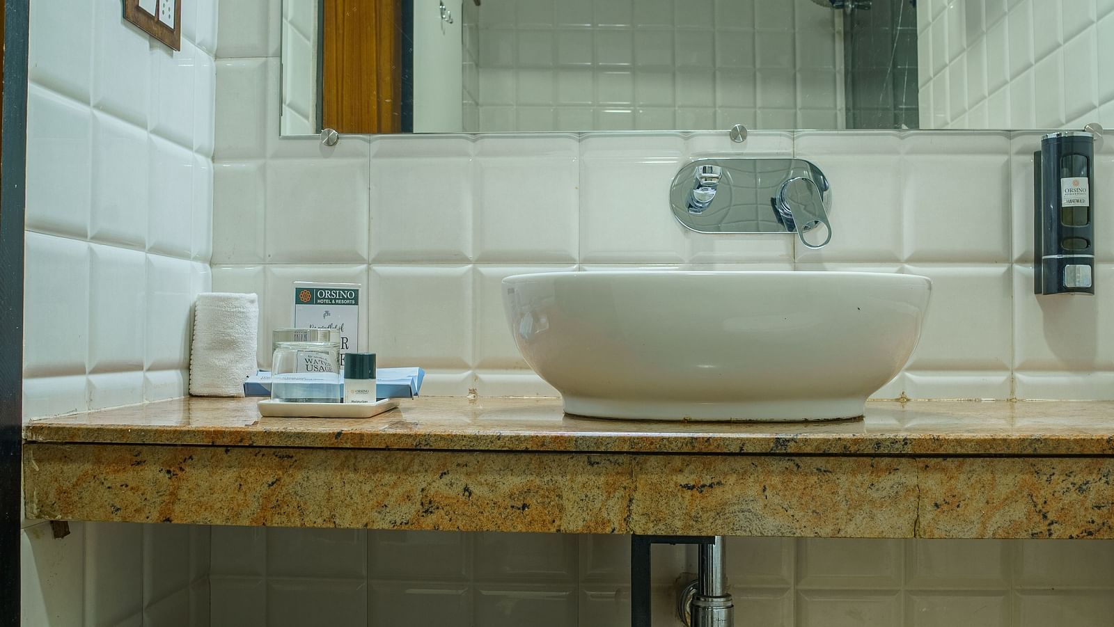 A bathroom at Orsino Spa Resort with a white sink, a mirror, and a shelf beneath the sink.
