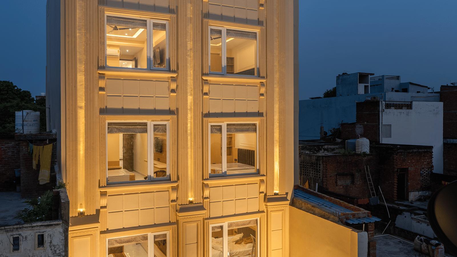 Front facade of Perfectstayz Premium Lavender, Varanasi at dusk, a cream 5-storey building with fluted pilasters, warm uplighting, and a glass entrance door.