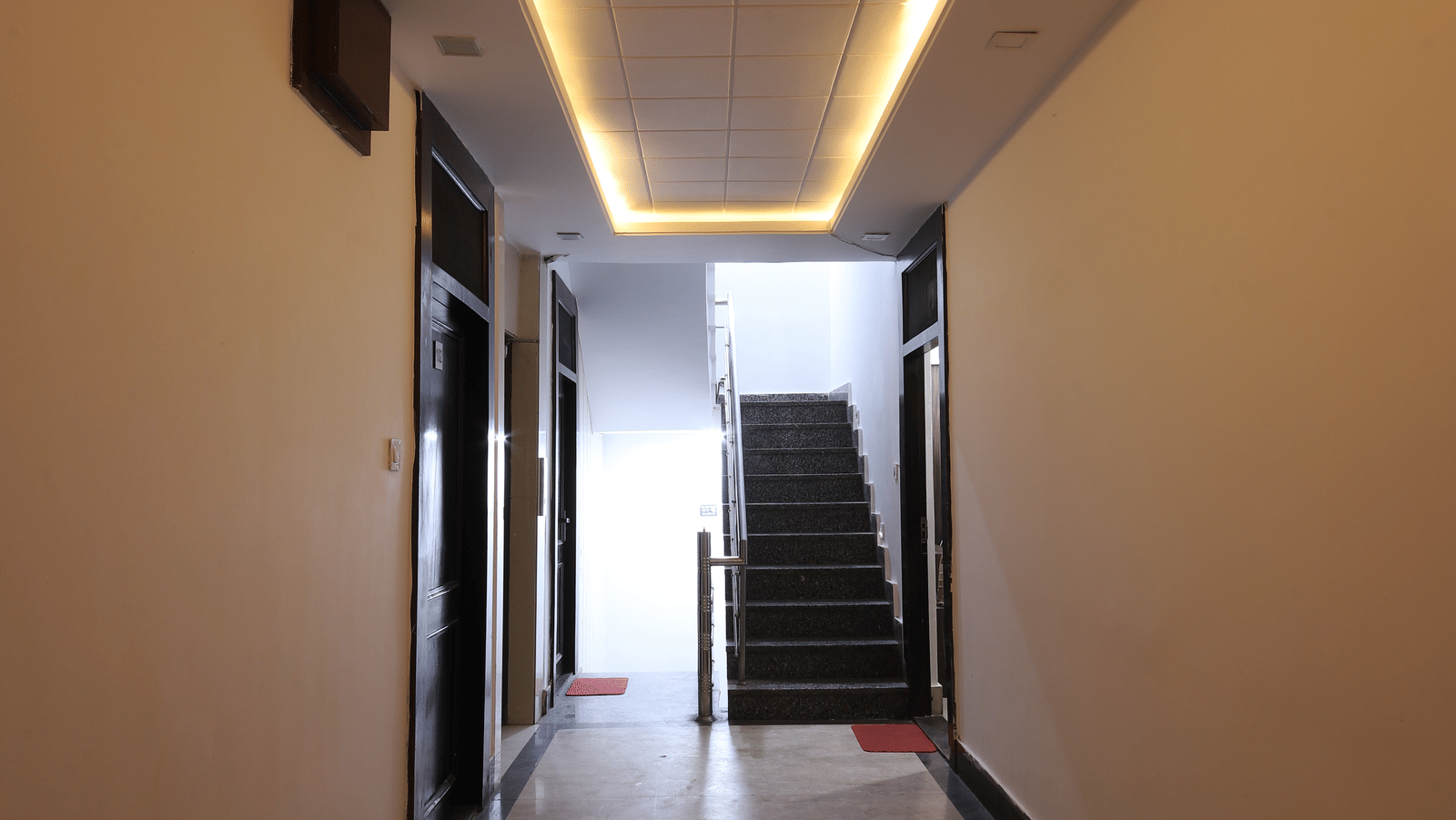 View down a simple hotel corridor with overhead lighting strips and plain walls - Perfectstayz Value Grey Castle, Haridwar