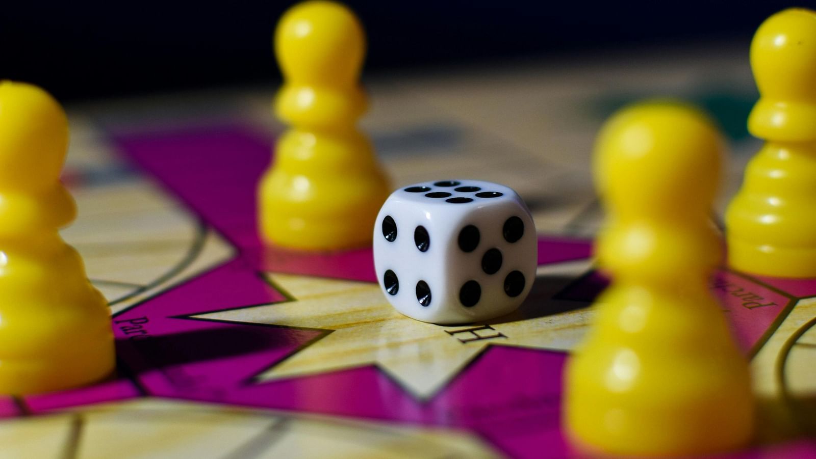 A close-up shot of a Ludo game board with yellow pawns and a die showing five pips.