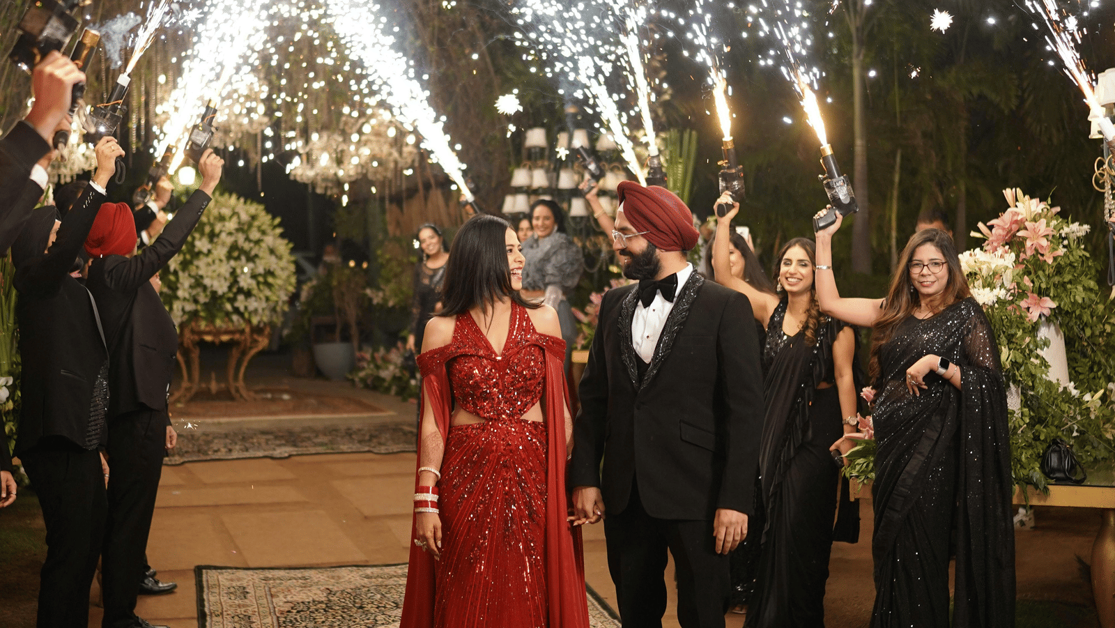 A couple holding hands while the best men and bridesmaids fire sparklers