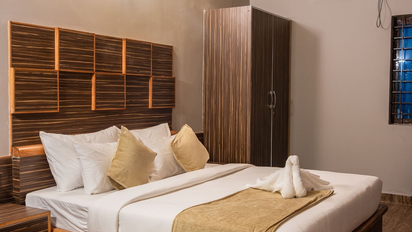 A comfortable bedroom is furnished with a large bed featuring a wooden headboard, soft lighting, and a view of the room's interior | Standard Room | RD's Nature Retreat, Bangalore