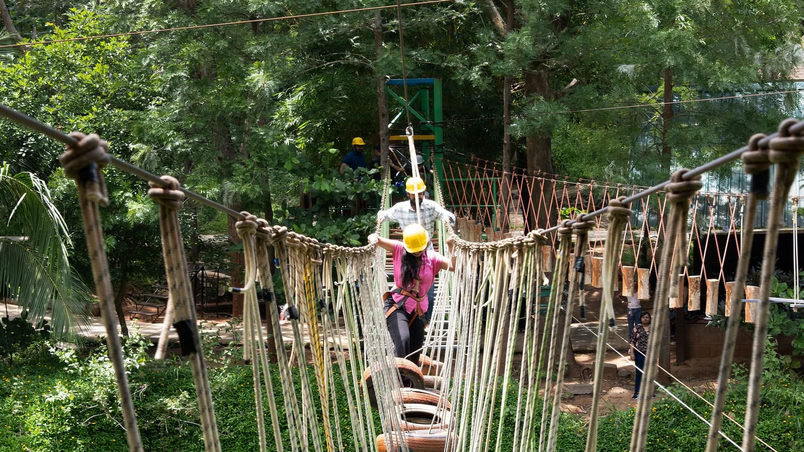 A person navigates a rope course with suspended wooden planks in a forest environment | RD's Nature Retreat, Bangalore