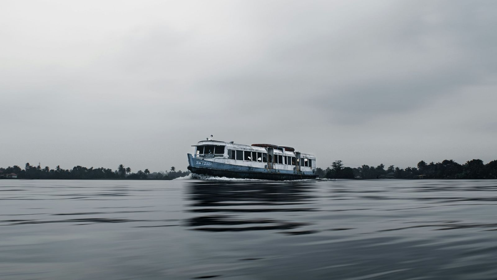 A solitary boat travelling on Vembanad lake in Kumarakom with white clouds in the sky.
