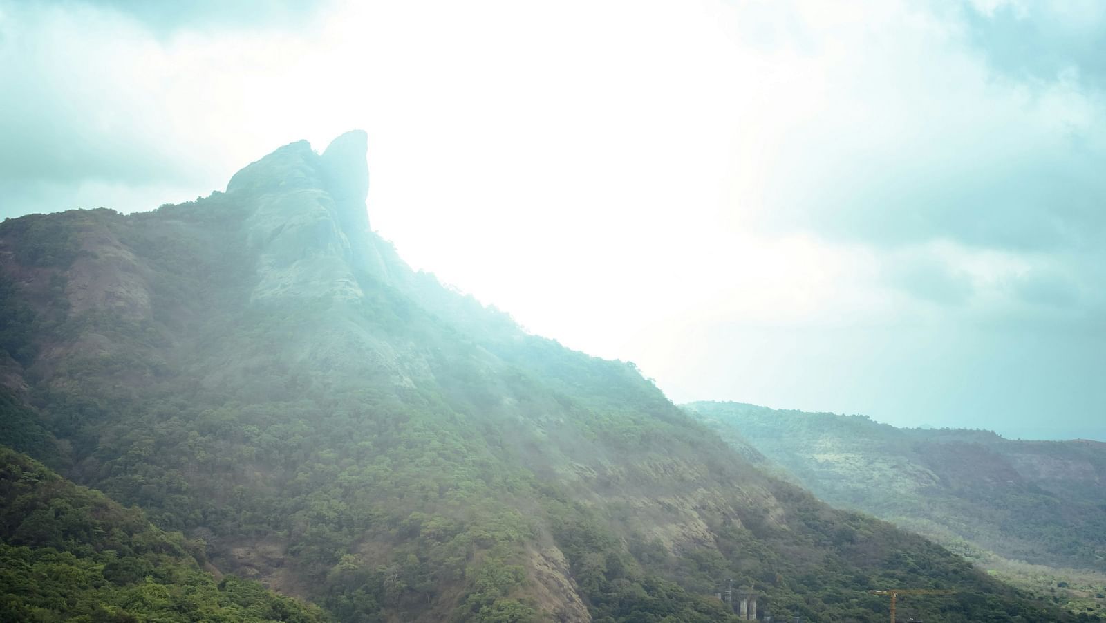 A view from a far of Lion's Point with greenery around and the sun shining above the peak.