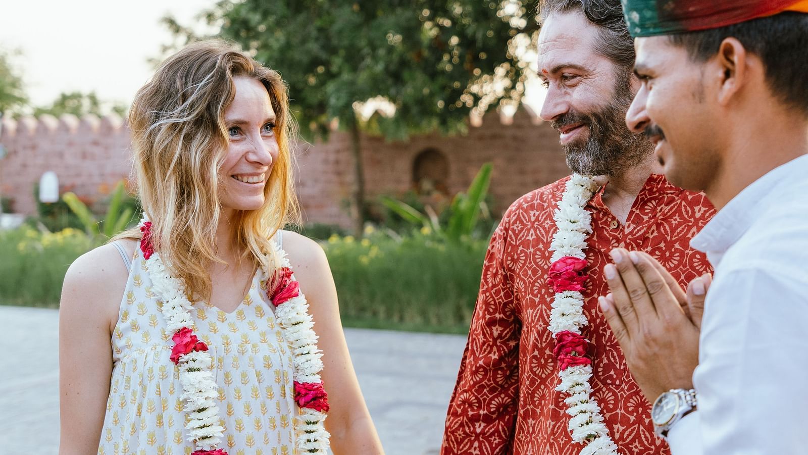 A man greeting two guests adorned with floral garland at Surpura Bagh.
