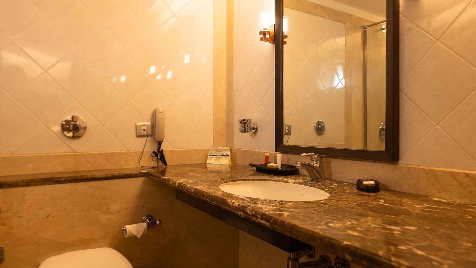 A long view of the bathroom with warm lighting and wall hanging mirror at The President Hotel Jayanagar, Bangalore