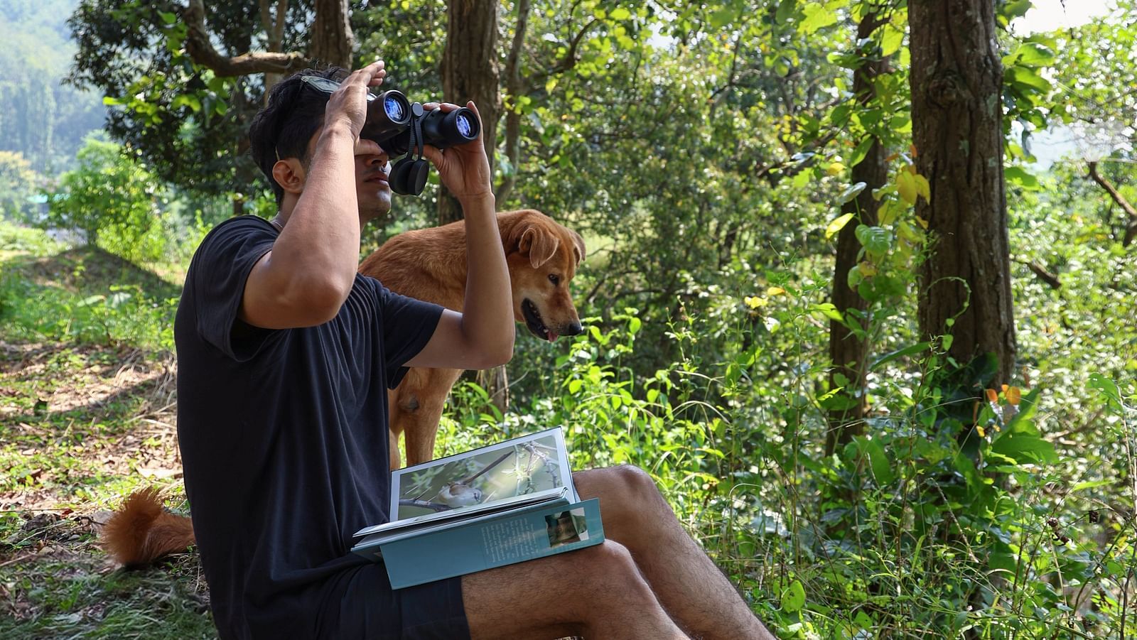 A man sitting on a cliff watching through binoculars at The Sylvan Retreat, Dehradun.