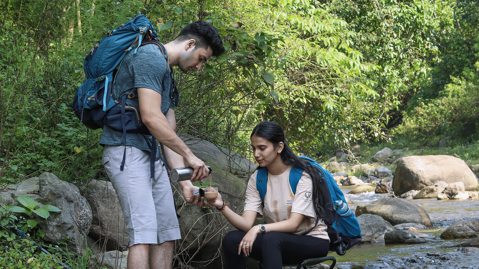 Two people resting on a rock alongside a water stream at the Sylvan Retreat, Dehradun.