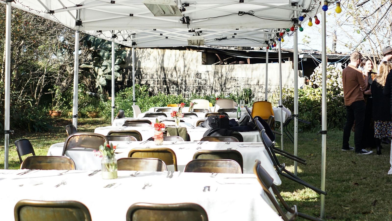 a shaded lawn area along with tables set with white table cloth along with folding chairs