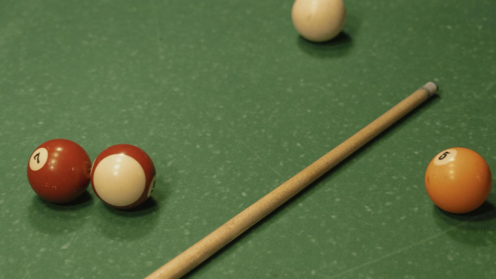 A green pool table with balls scattered and a cue stick placed on it.