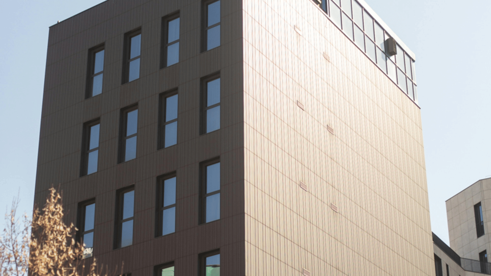 A tall rectangular building with rows of windows stands against a clear sky.