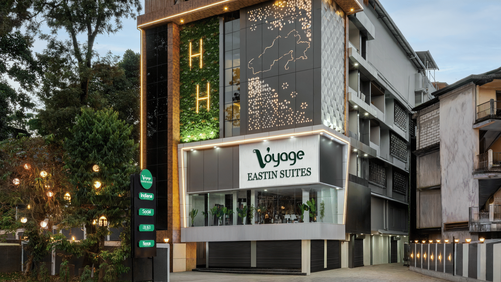The exterior of a multi-storey hotel building with large windows and an entrance on the ground floor, surrounded by trees and greenery | Voyage Eastin Suites