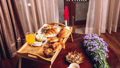 Breakfast spread on a table by the window with tea, juice, fruits, and pastries.
