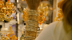 A person is shown from the side, looking at a brightly lit display of gold jewellery inside a shop