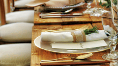 A long wooden table with beautifully set cutlery with small fern leaves in vases.
