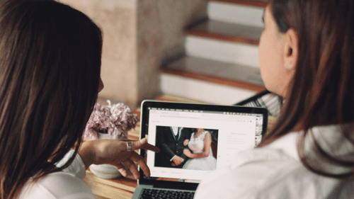A wedding planner and a bride looking at pictures of a wedding on the laptop.