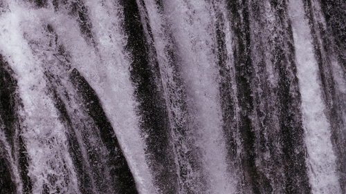 A powerful waterfall plunges down jagged rocks, creating a curtain of white water against a dark cliff.