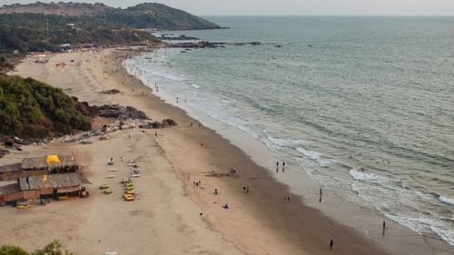 Long shot of a sea shore with many people, water scooters parked, and shacks.
