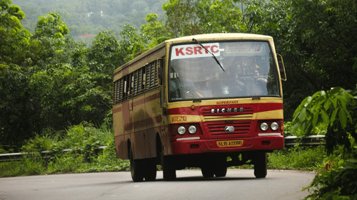A red bus driving on a winding road through a hilly, forested area.