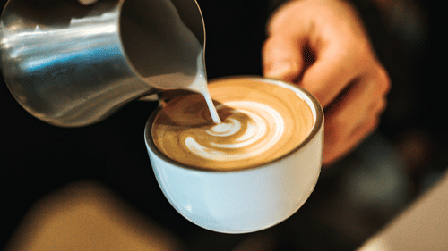 A barista pouring cream in a cup of coffee