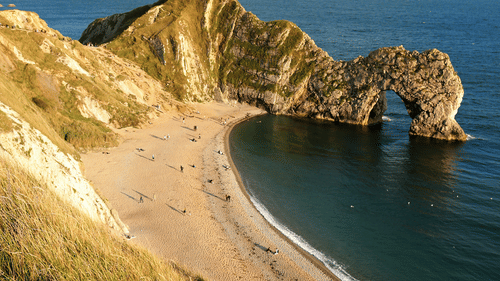 A natural formation of rocks near a beach with white clouds on blue sky in the background