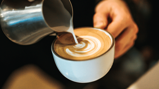 A barista pouring cream in a cup of coffee