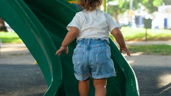 A kid walking up a green slide during the day