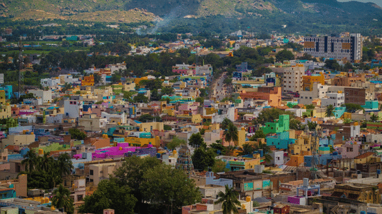  An aerial view shows a densely packed, colorful city situated in a valley with a river and mountains in the distance.