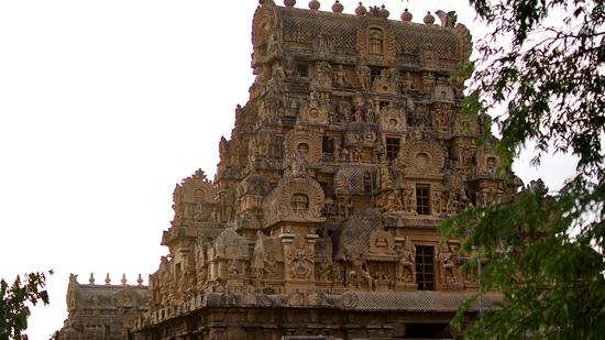 A large, ancient stone temple with multiple tiers and intricate carvings is partially visible through green foliage.