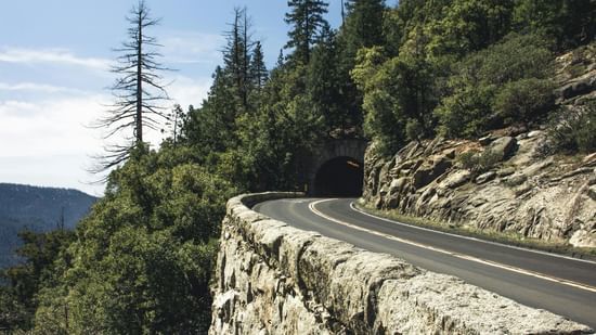Highway route passing through the tunnel amidst the hilly slopes under a partly clouded sky.
