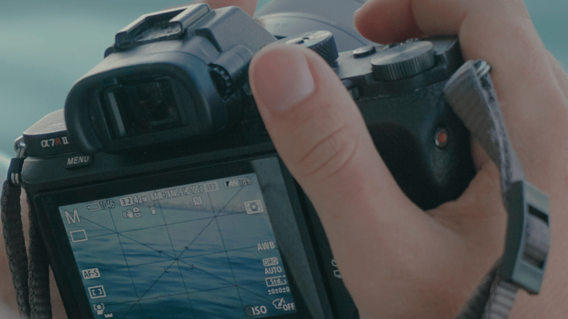 A photographer holds a camera, capturing a scenic view of water.