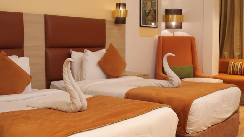 Twin room with orange pillows, wooden headboards, white linens and modern ceiling design at Best Western, Vrindavan.