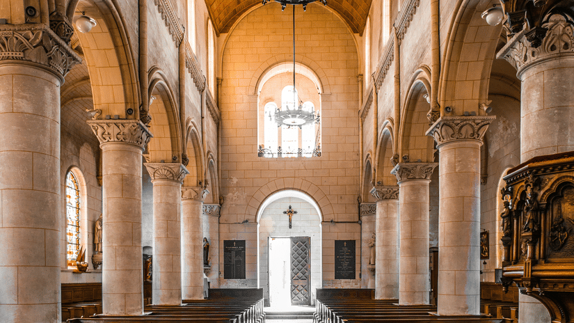 A view of the interior of a church with seatings on either side, a platform in the background, and a chandelier above.