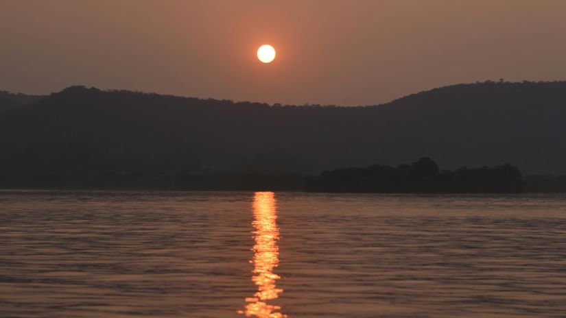 The sun sets above distant hills, casting a reflection across the surface of a body of water.