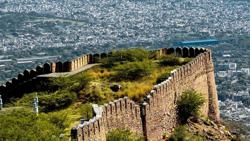 A scenic view of an ancient fort on a hilltop, overlooking a city with distant mountains in the background.