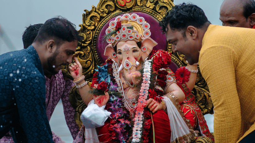Devotees gather around a colourful Ganesha idol during a traditional immersion ceremony by the water.