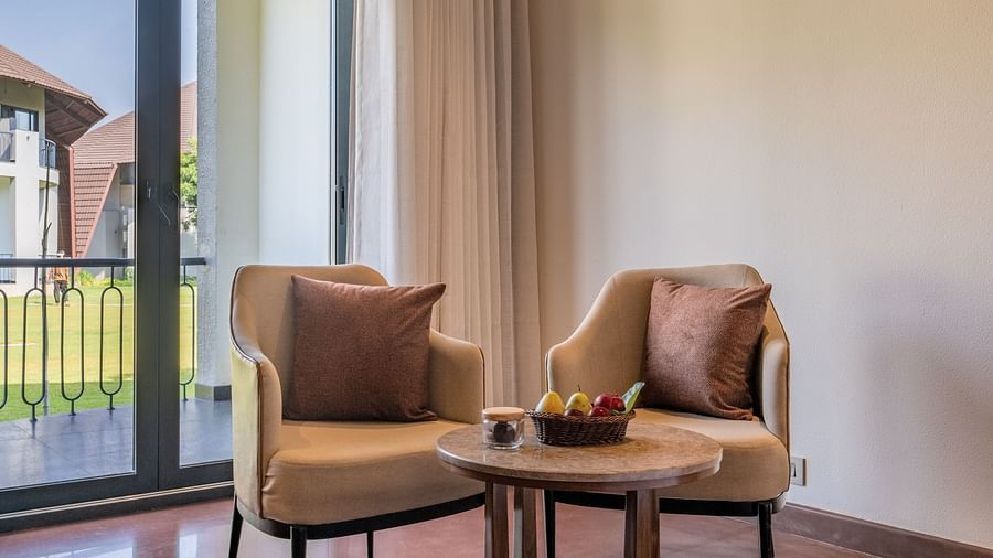 An image of a seating area with two chairs and a tea table with a backdrop of a window from where natural light is flooding the room