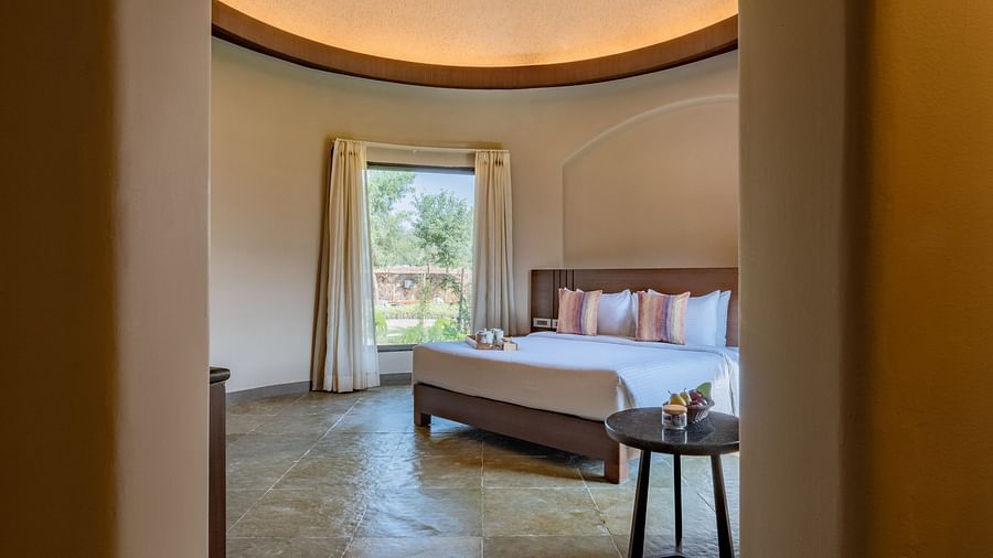 A sneak peak image of a room with bedroom with a tea table and a large window from where sunlight is flooding